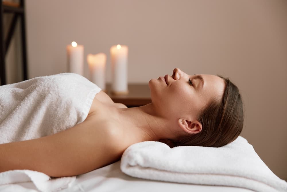 A client relaxing under a soft towel during the 5 Zenses Massage at The Zen Den, surrounded by a warm candlelit ambiance for deep relaxation and sensory balance.