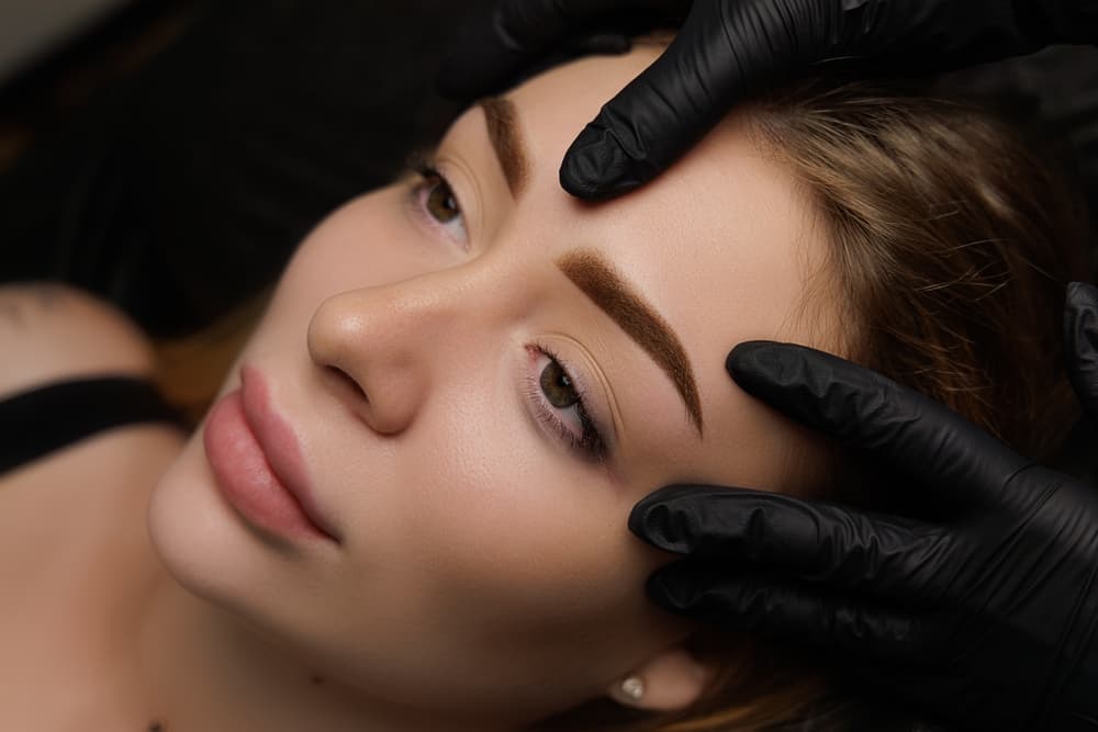 Close-up of a client during a brow consultation at The Zen Den, with a beauty professional wearing black gloves gently assessing eyebrow shape.