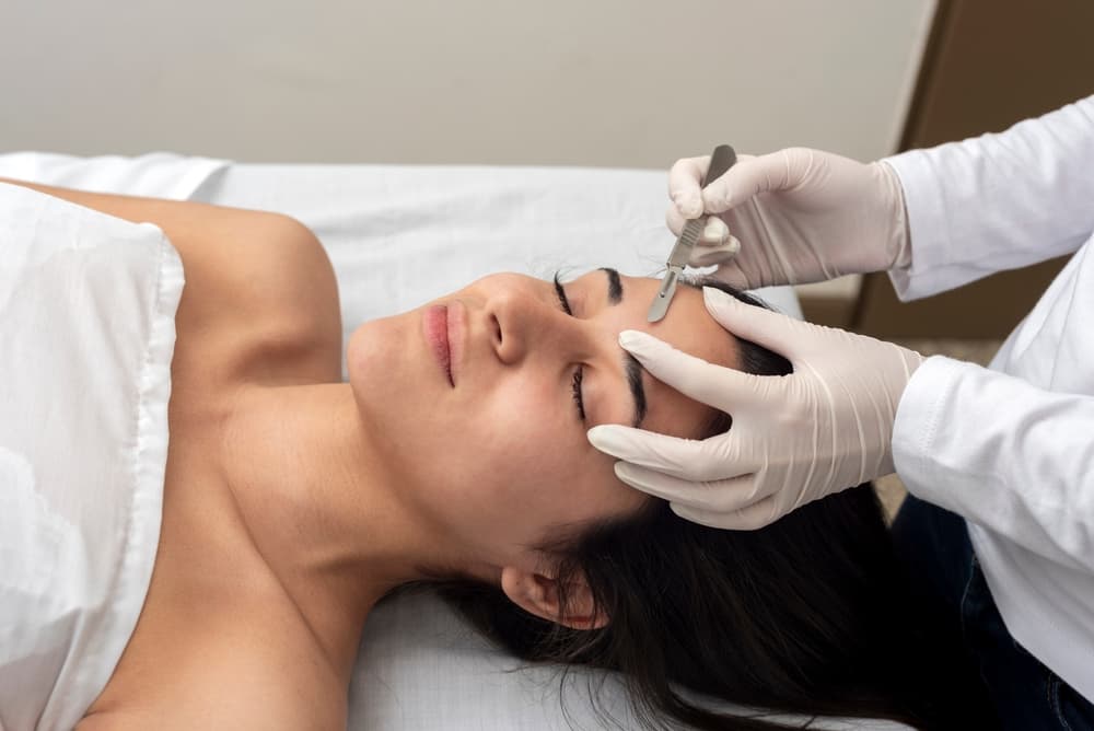 A client receiving a professional dermaplaning treatment at The Zen Den to exfoliate the skin and remove peach fuzz.