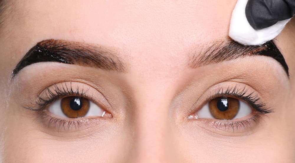 Close-up of a beauty therapist applying eyebrow tint with a cotton pad to enhance and define the client's brows during an eyebrow tint treatment at The Zen Den.