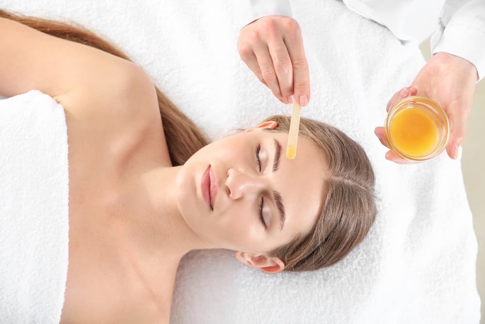 Beauty therapist applying warm wax to a client’s eyebrows using a wooden spatula during an eyebrow waxing treatment at The Zen Den.