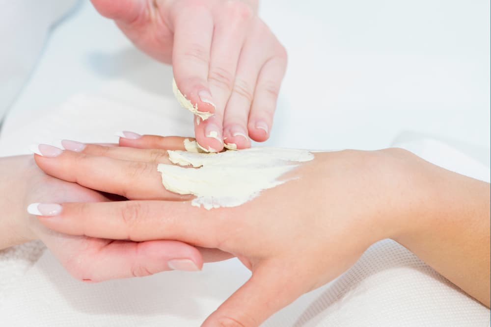 Close-up of a beauty therapist applying a creamy hand mask treatment onto the back of a client’s hands, focusing on hydration and skin nourishment, representing The Zen Den's Hand Mask Add-On service.