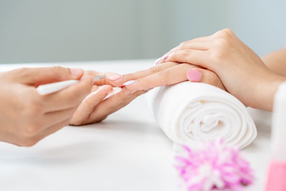 Close-up of a beauty therapist performing a manicure, gently pushing back cuticles on neatly shaped nails, with the client’s hands resting on a rolled white towel, representing The Zen Den's Healthy Hands Manicure service.        Ask ChatGPT