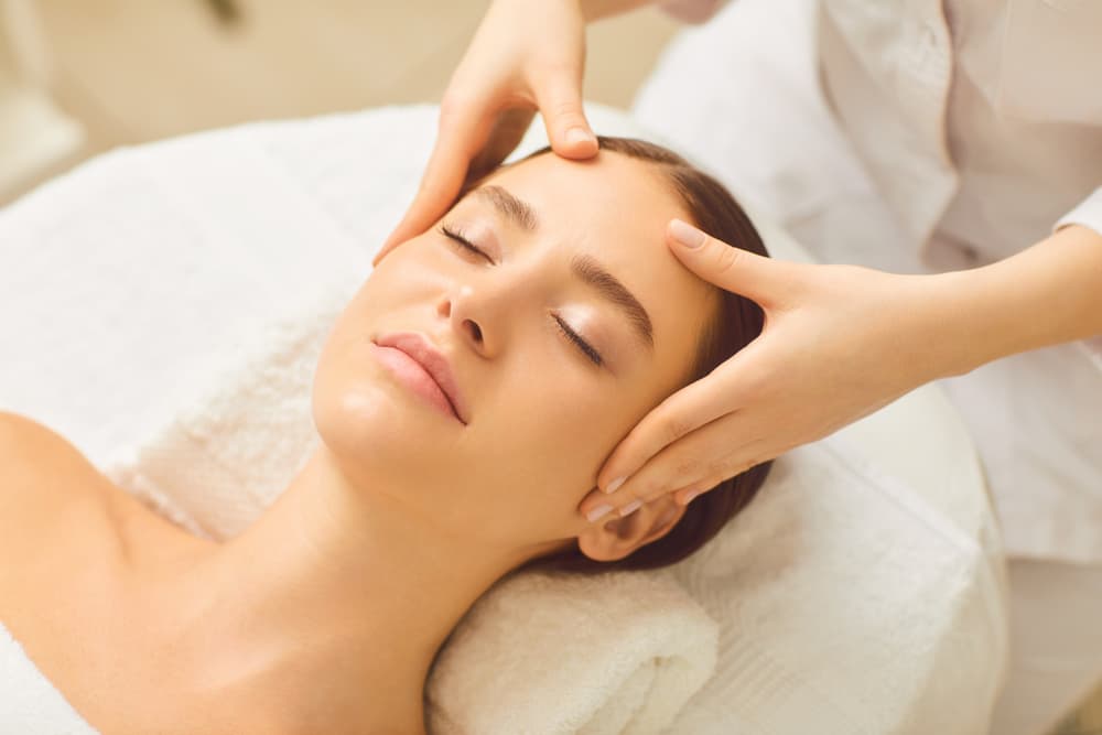 Woman lying comfortably with eyes closed, receiving a relaxing head massage at The Zen Den, promoting deep relaxation and relief from tension