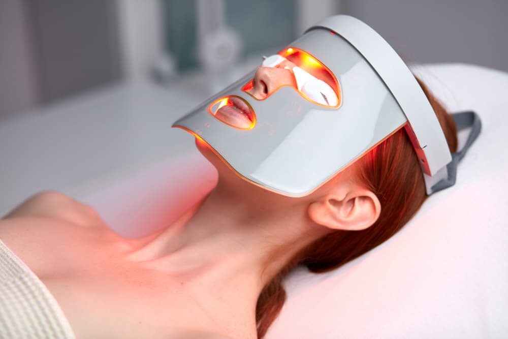 A client relaxing under an LED light therapy mask at The Zen Den, a treatment that targets skin concerns like ageing, breakouts, and dullness using red light technology.