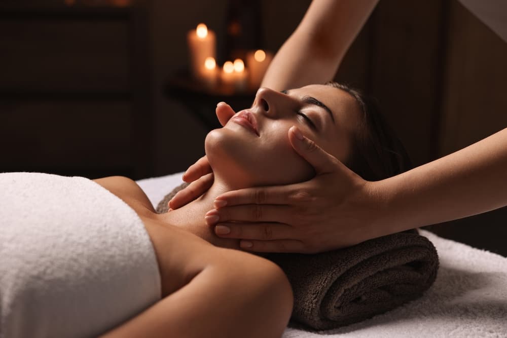 Woman relaxing with eyes closed during a soothing mini facial massage at The Zen Den, with candlelight creating a calming spa atmosphere.
