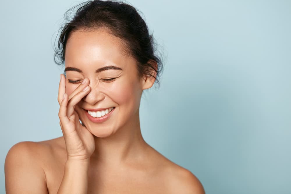 Smiling woman with glowing, luminous skin touching her face after a Radiance Facial treatment at The Zen Den.