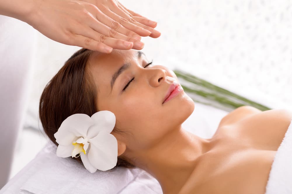 Woman relaxing with eyes closed during a Reiki healing session at The Zen Den @ Watt A Beauty in Glasgow, with a white orchid in her hair.