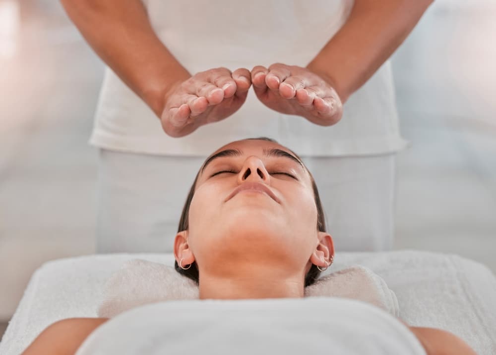 Woman relaxing during a Reiki session at The Zen Den @ Watt A Beauty in Glasgow, with hands hovering above her head to channel healing energy.