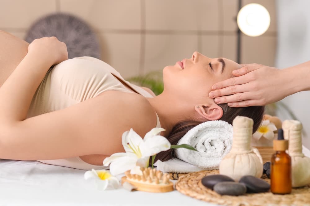 Pregnant woman enjoying a relaxing facial and head massage with reiki, flowers, and natural oils during a calming pregnancy spa treatment.