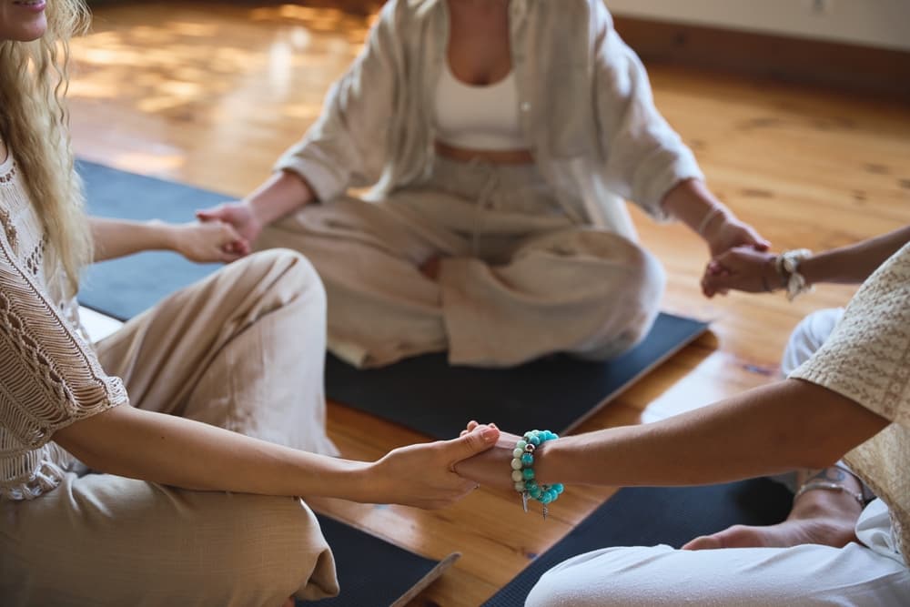 Group sitting in a circle holding hands during a mindful workshop at The Zen Den in Glasgow, symbolising connection, calm, and community.