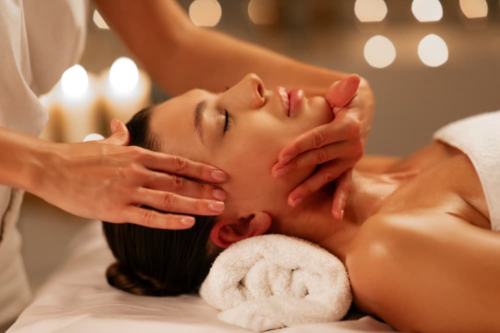 A calming uplifting facial massage at The Zen Den, with a therapist gently massaging the jawline and temples to promote relaxation and a radiant glow.