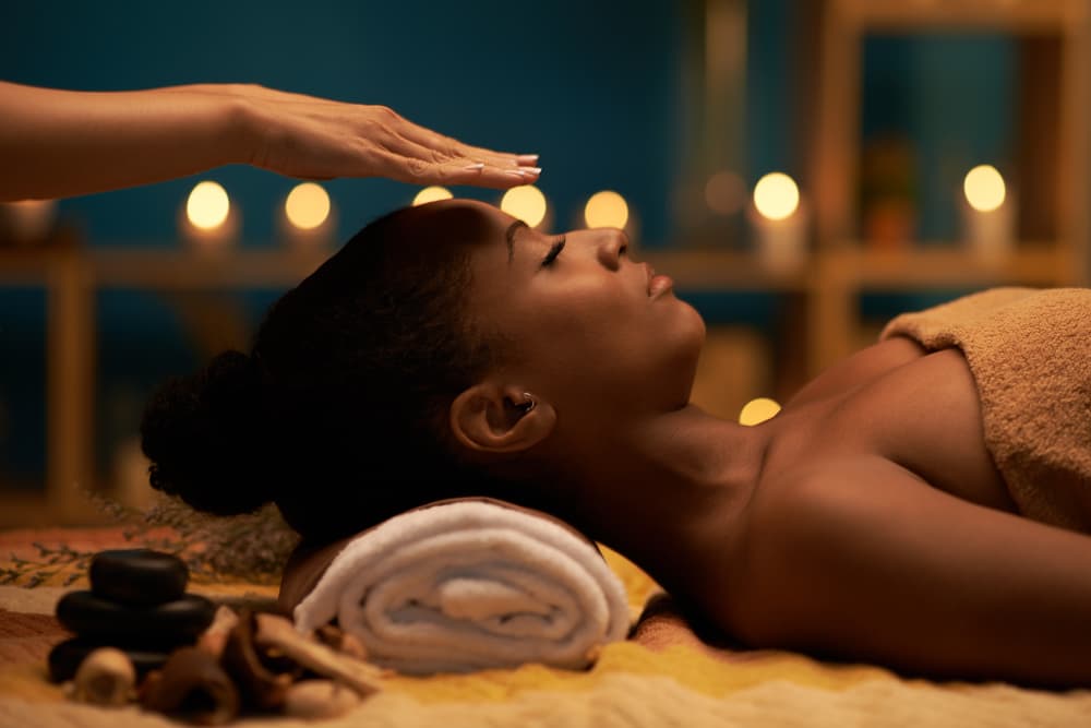 Woman receiving Reiki healing during Watt A Vibe treatment with relaxing candles, LED facial benefits, and balancing massage at The Zen Den.